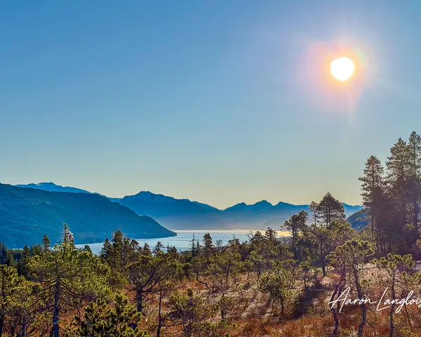 Sun shining above distant mountain ranges and calm water